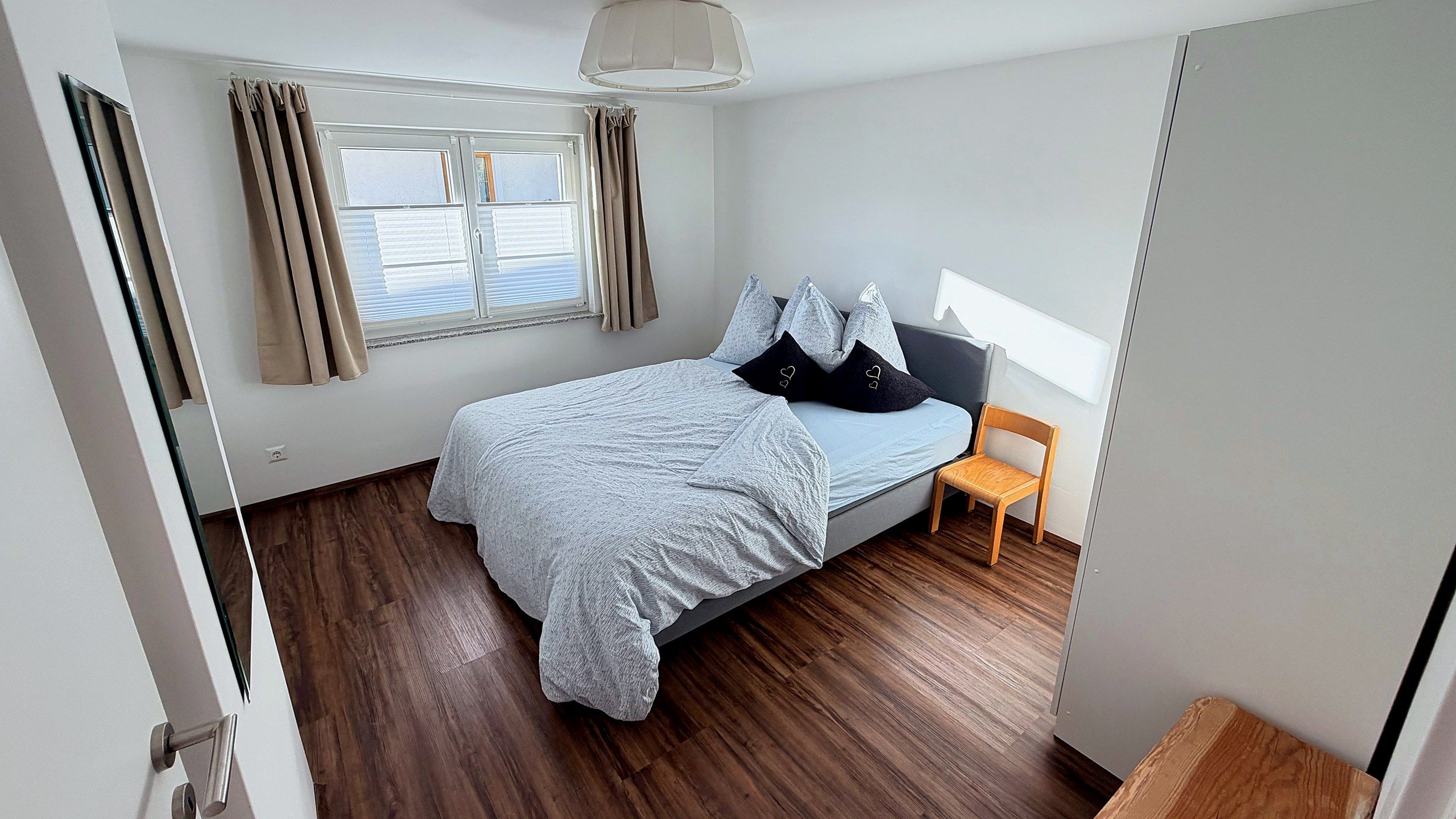 Zweites Schlafzimmer mit Doppelbett, hellgrauer Bettwäsche und Holzstuhl